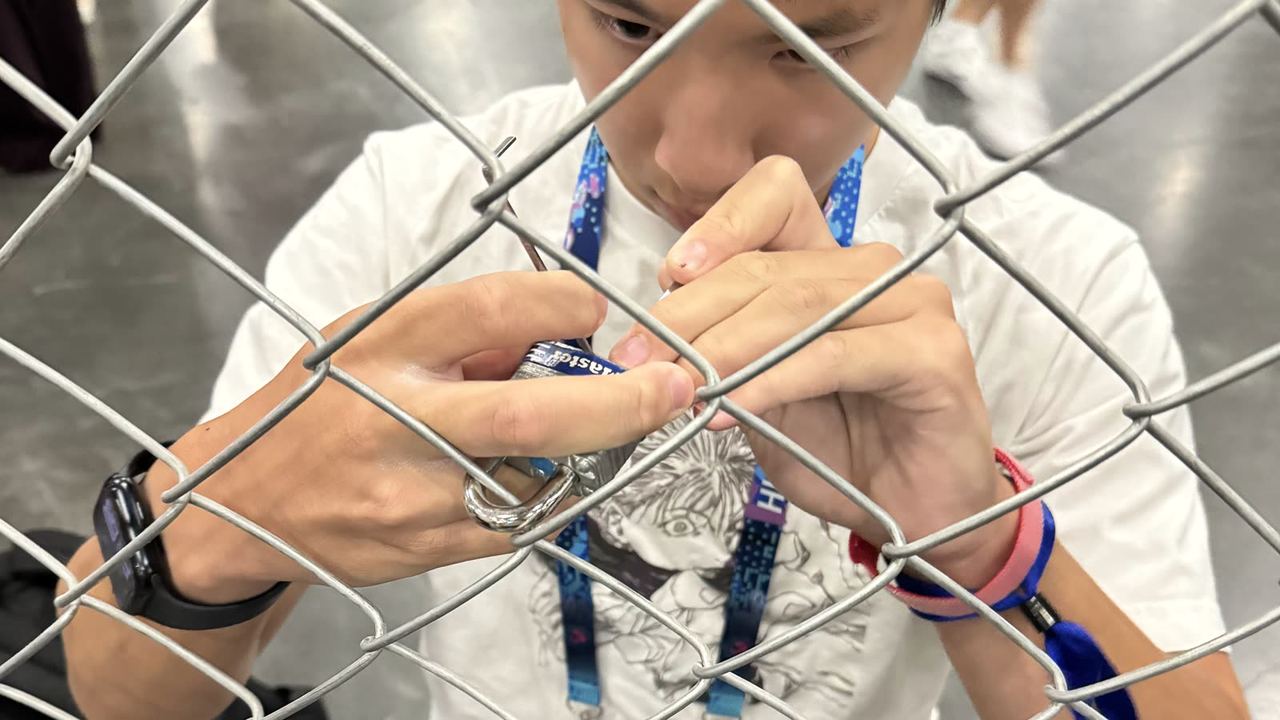 A club member working a lock through a chain-link fence during a lockpicking challenge