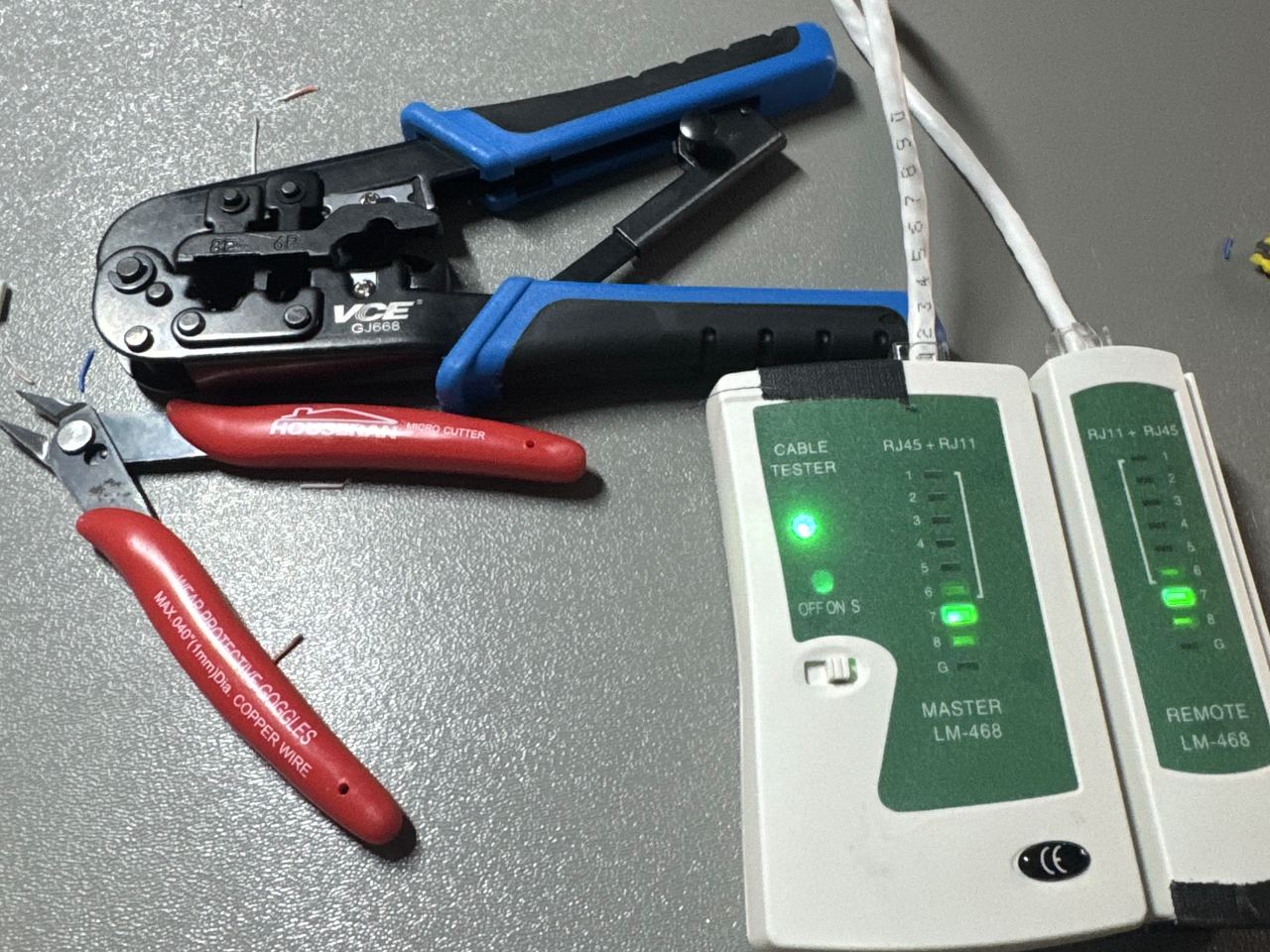 A crimping tool, wire cutters, and a cable tester lighting up while checking a freshly made ethernet cable